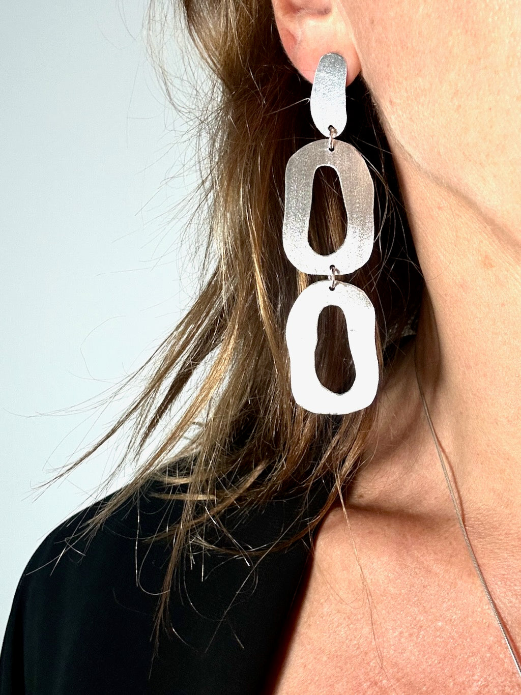 Long dangly organic oval silver earrings worn, shown on ear