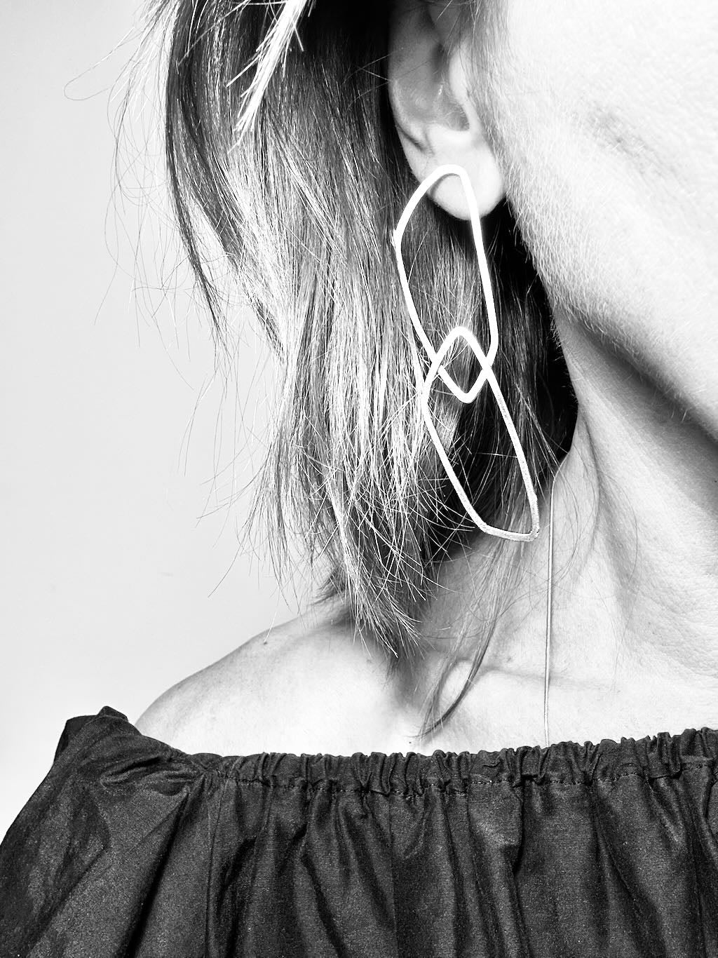 Black and white photo of long angular silver link earrings worn on the ear