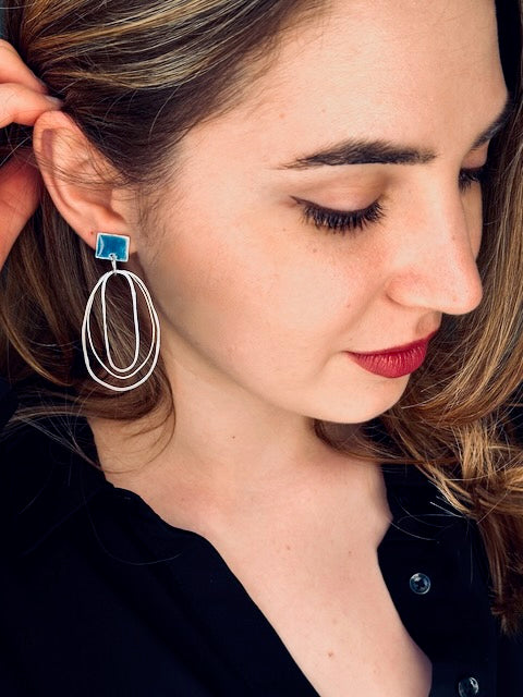 Pair of contemporary sterling silver statement earrings with multiple oval hoops and bold blue resin square studs worn on model