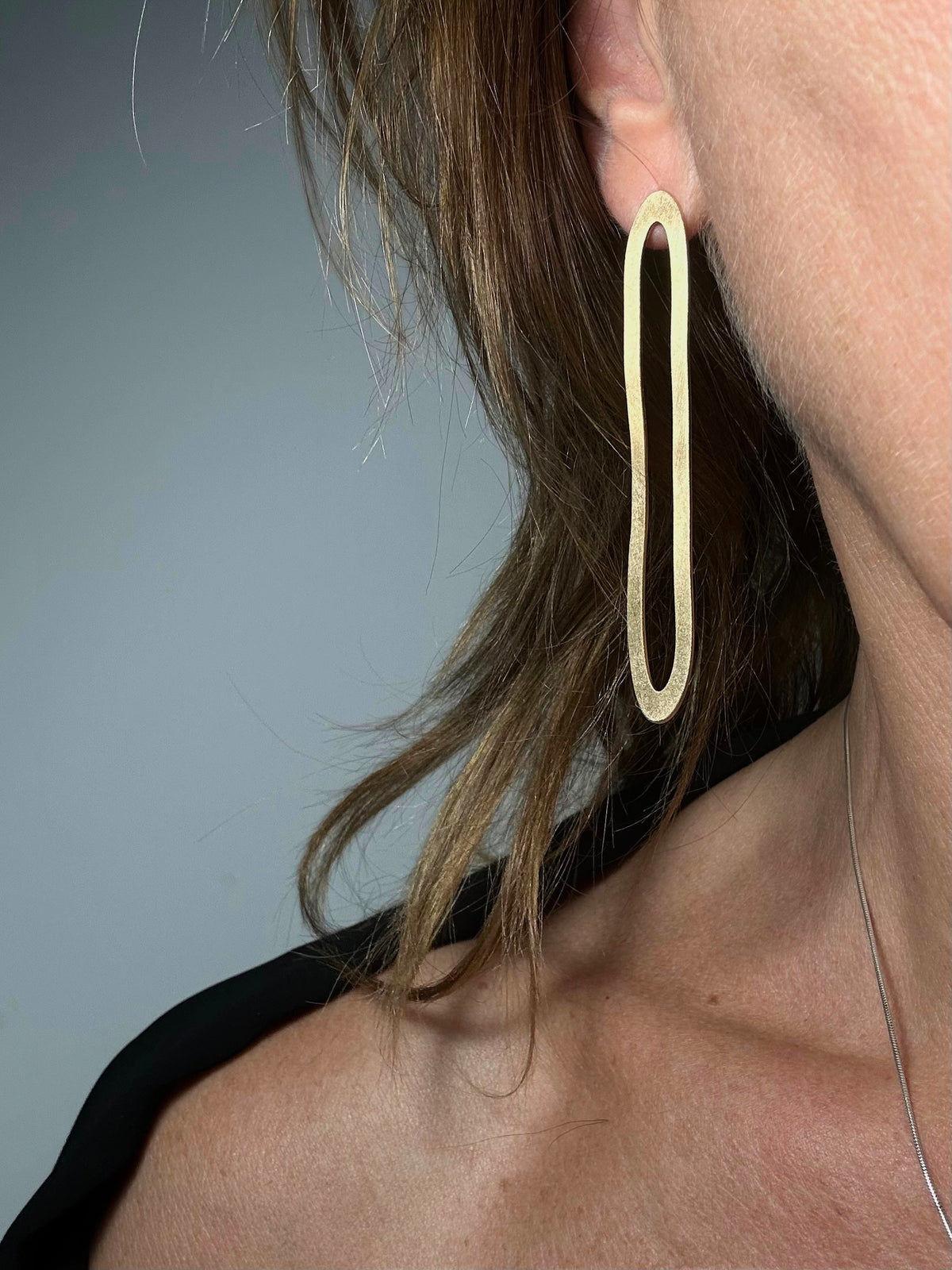 Model wearing large gold oval hoop earring, close-up