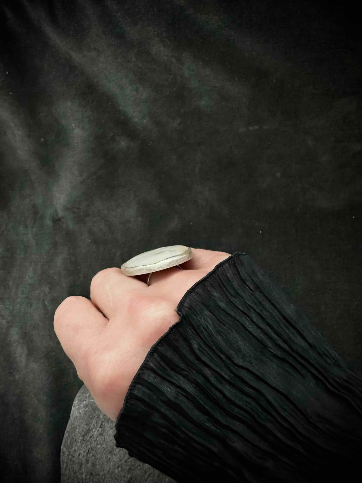 Low angle view of oversized nacre ring on finger, black sleeve