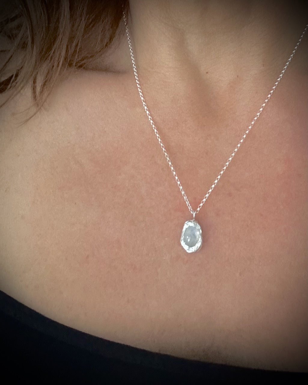 Minimalist sterling silver moonstone necklace with oval gemstone and sculptural nugget setting on a person's neck