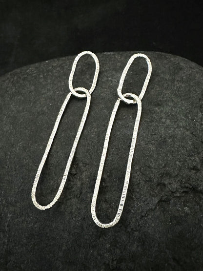 Long oval dangly hammered silver earrings laid on dark stone