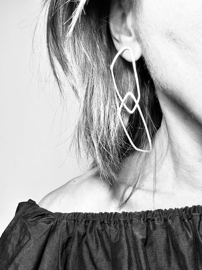 Black and white photo of long angular silver link earrings worn on the ear
