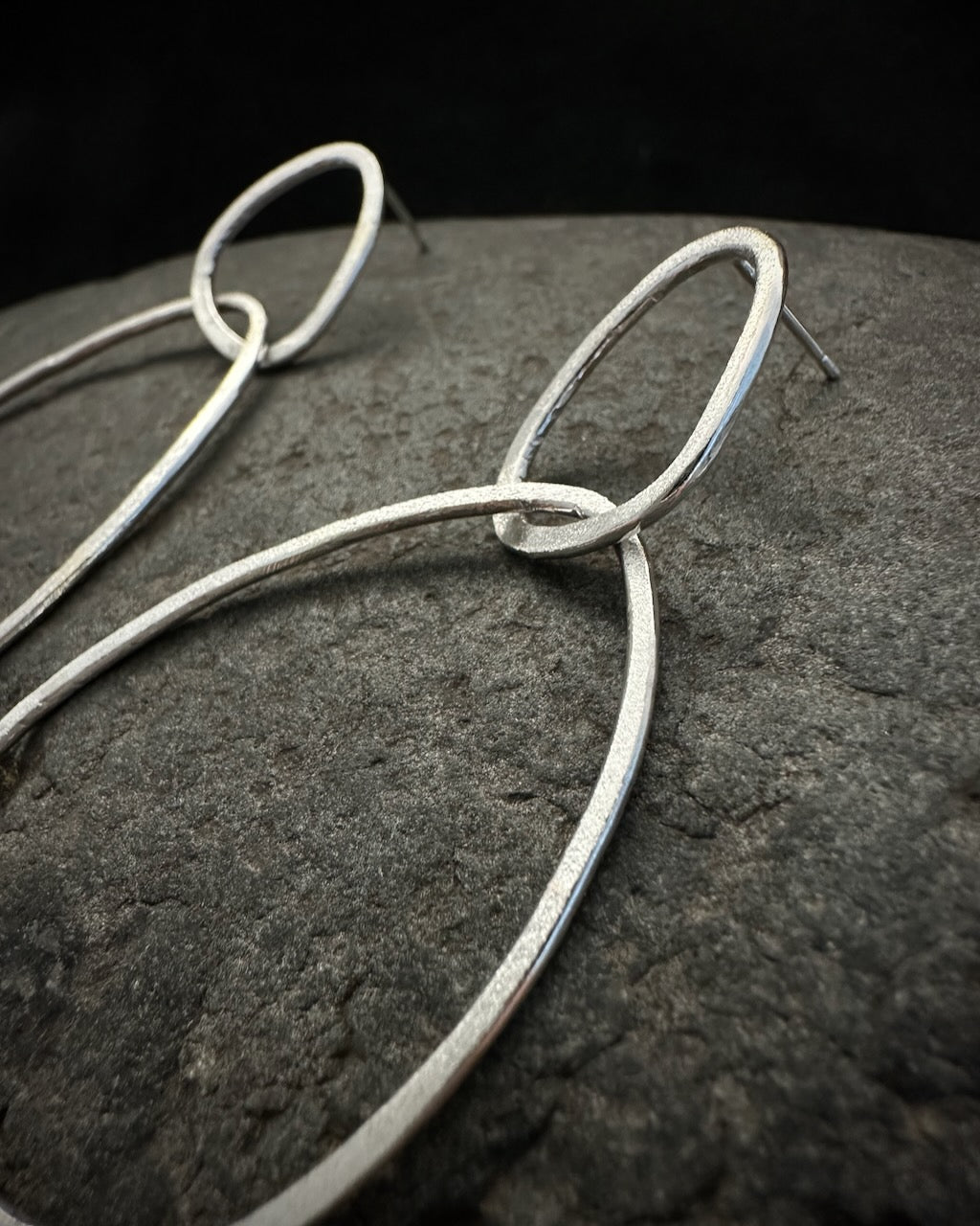 Close-up of handcrafted sterling silver drop earrings with textured satin finish