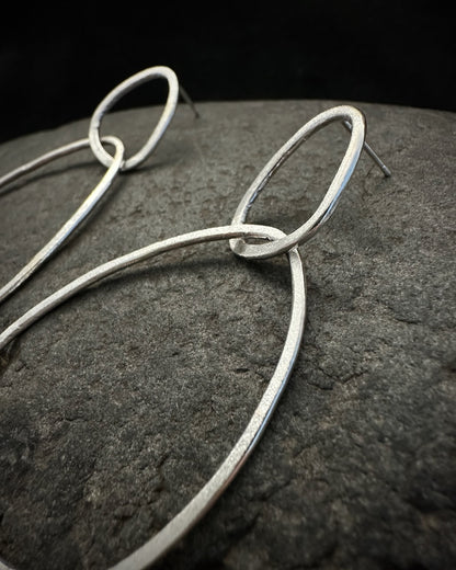 Close-up of handcrafted sterling silver drop earrings with textured satin finish