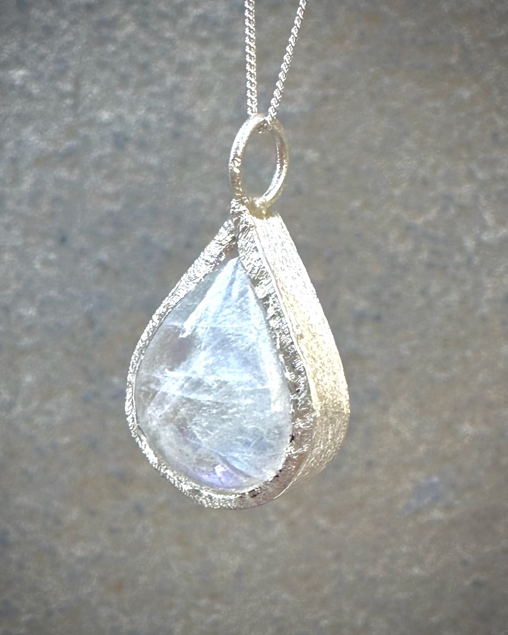 Teardrop-shaped moonstone pendant on a chain against a neutral background
