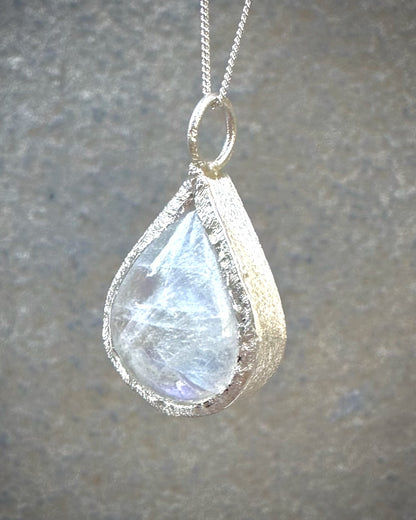 Teardrop-shaped moonstone pendant on a chain against a neutral background