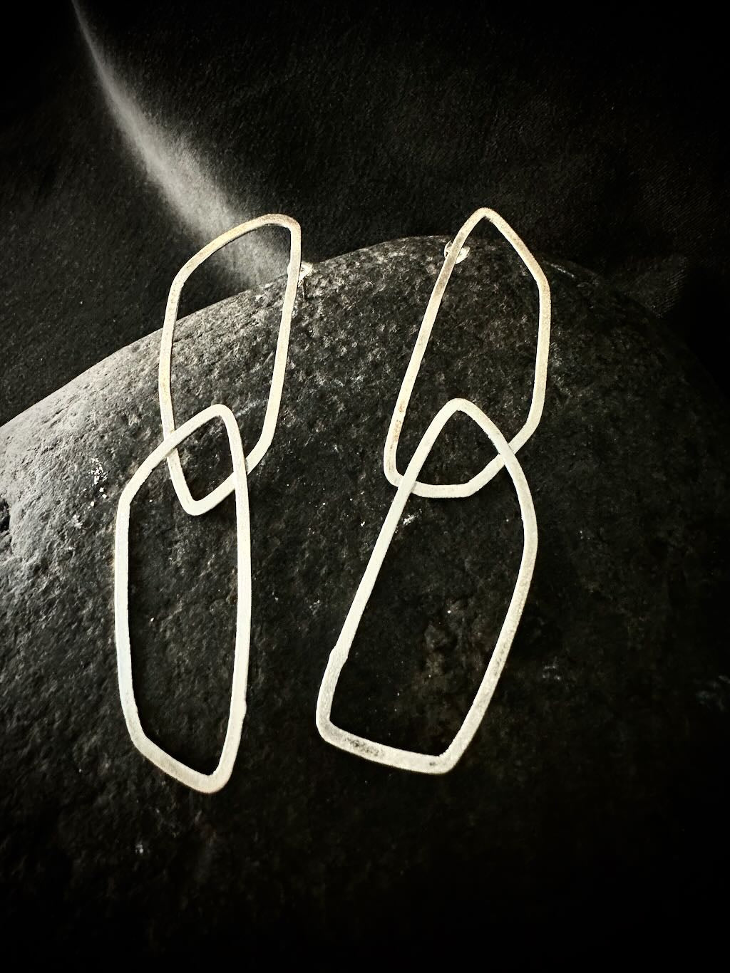 Pair of geometric sterling silver loop earrings on dark stone