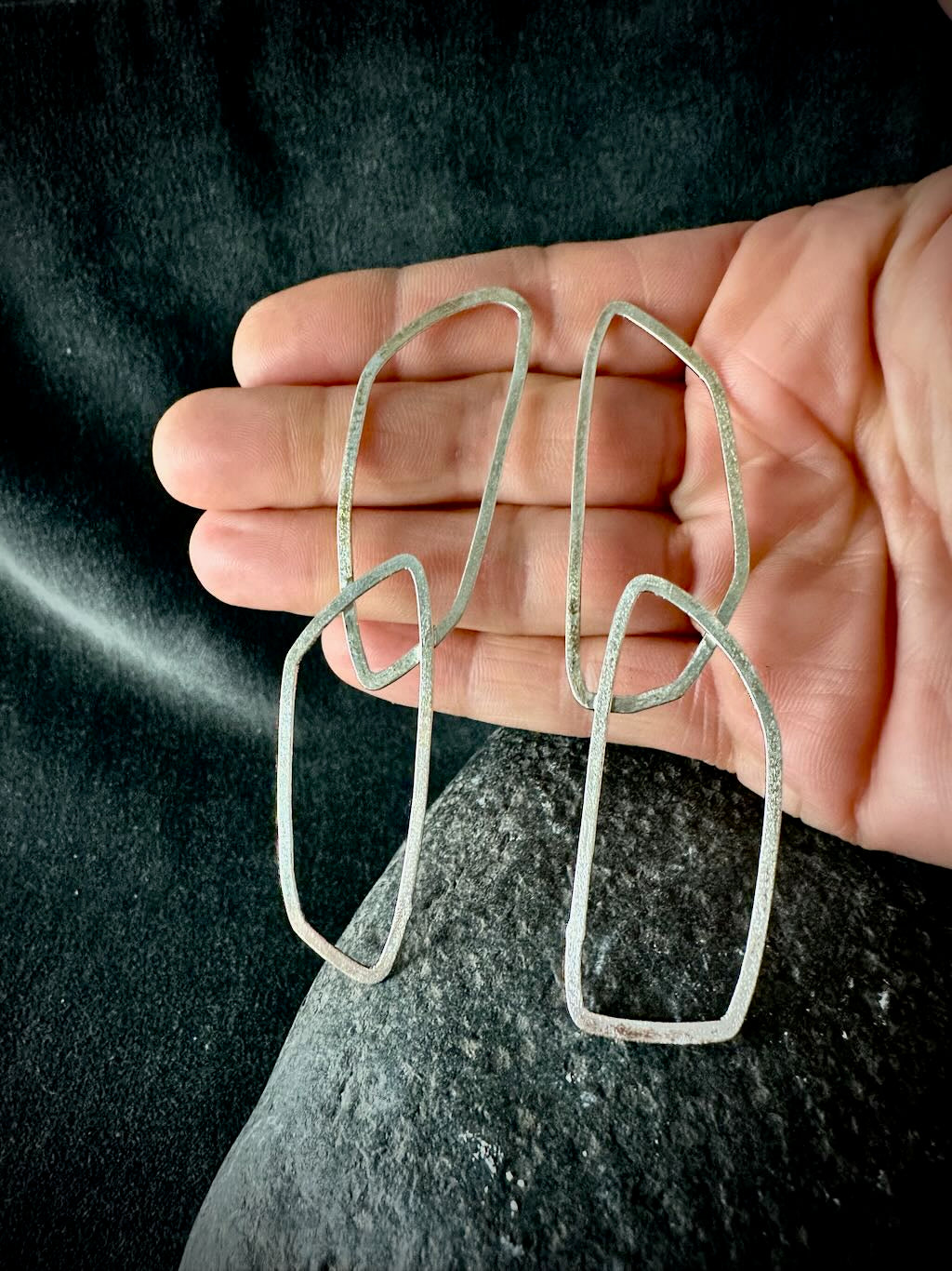 Handmade angular silver link earrings held in an open hand to show their scale