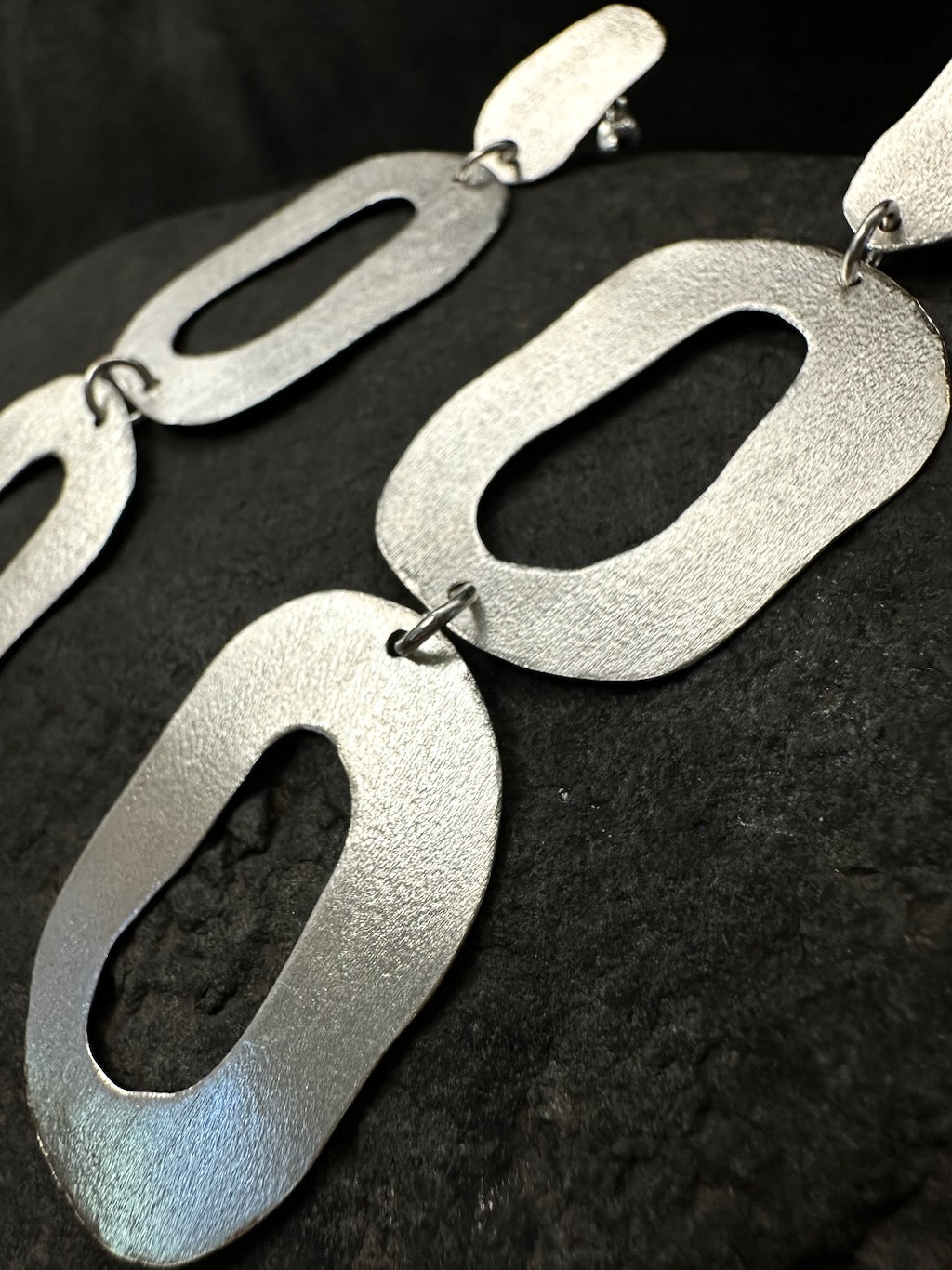 Close-up of brushed texture on organic oval silver earring shapes