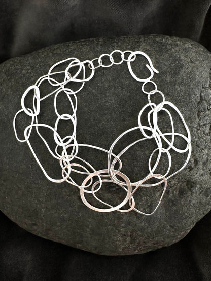 A chunky silver-toned link bracelet with elongated oval links, displayed on a dark textured stone against a black fabric background.