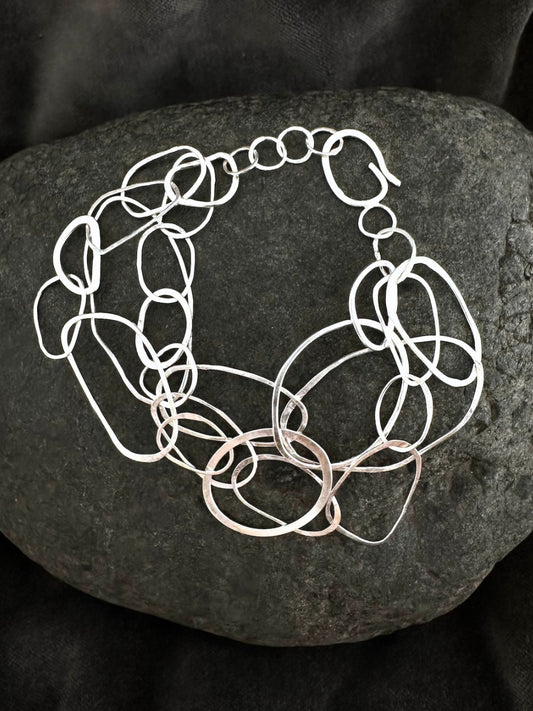 A chunky silver-toned link bracelet with elongated oval links, displayed on a dark textured stone against a black fabric background.