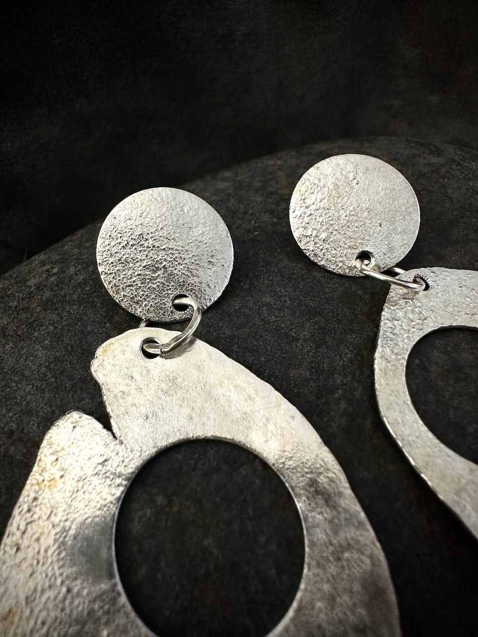 Close-up of handmade silver earrings. Reticulated surface detail, jump ring connection, organic hoop with raw irregular outer edge.