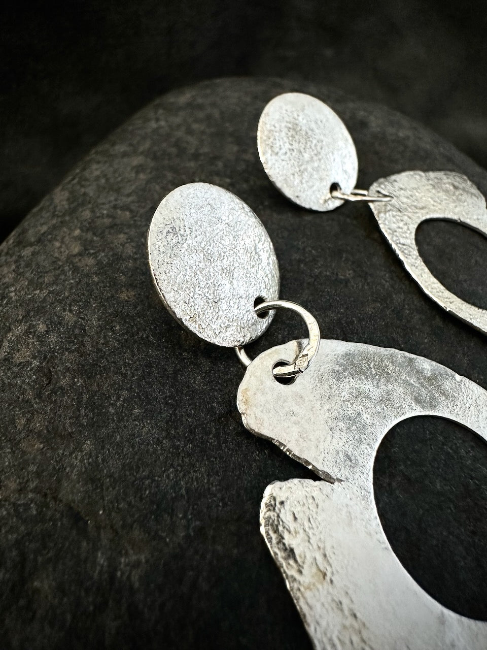 Handmade silver drop earrings, side view. Textured disc and organic open hoop in recycled sterling silver, irregular edge, matte finish.