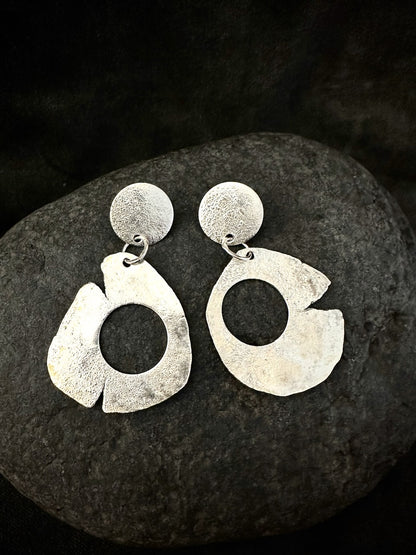 Pair of sculptural silver drop earrings on dark stone. Recycled sterling silver, matte textured disc and large organic open hoop, handmade in France.