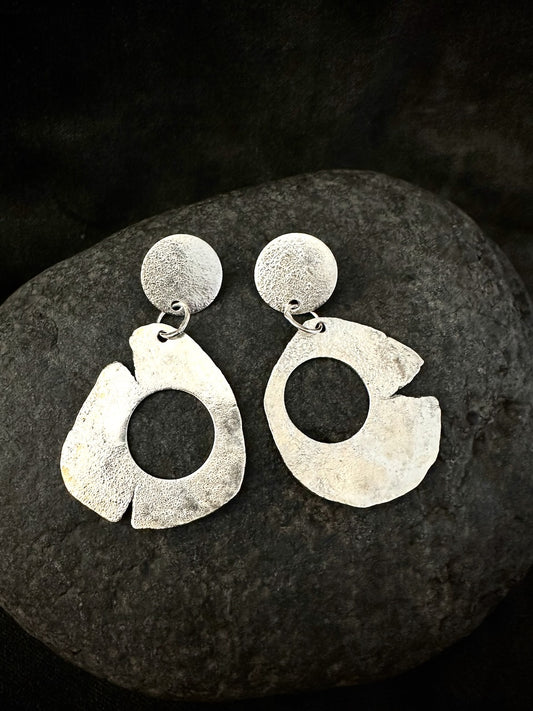 Pair of sculptural silver drop earrings on dark stone. Recycled sterling silver, matte textured disc and large organic open hoop, handmade in France.