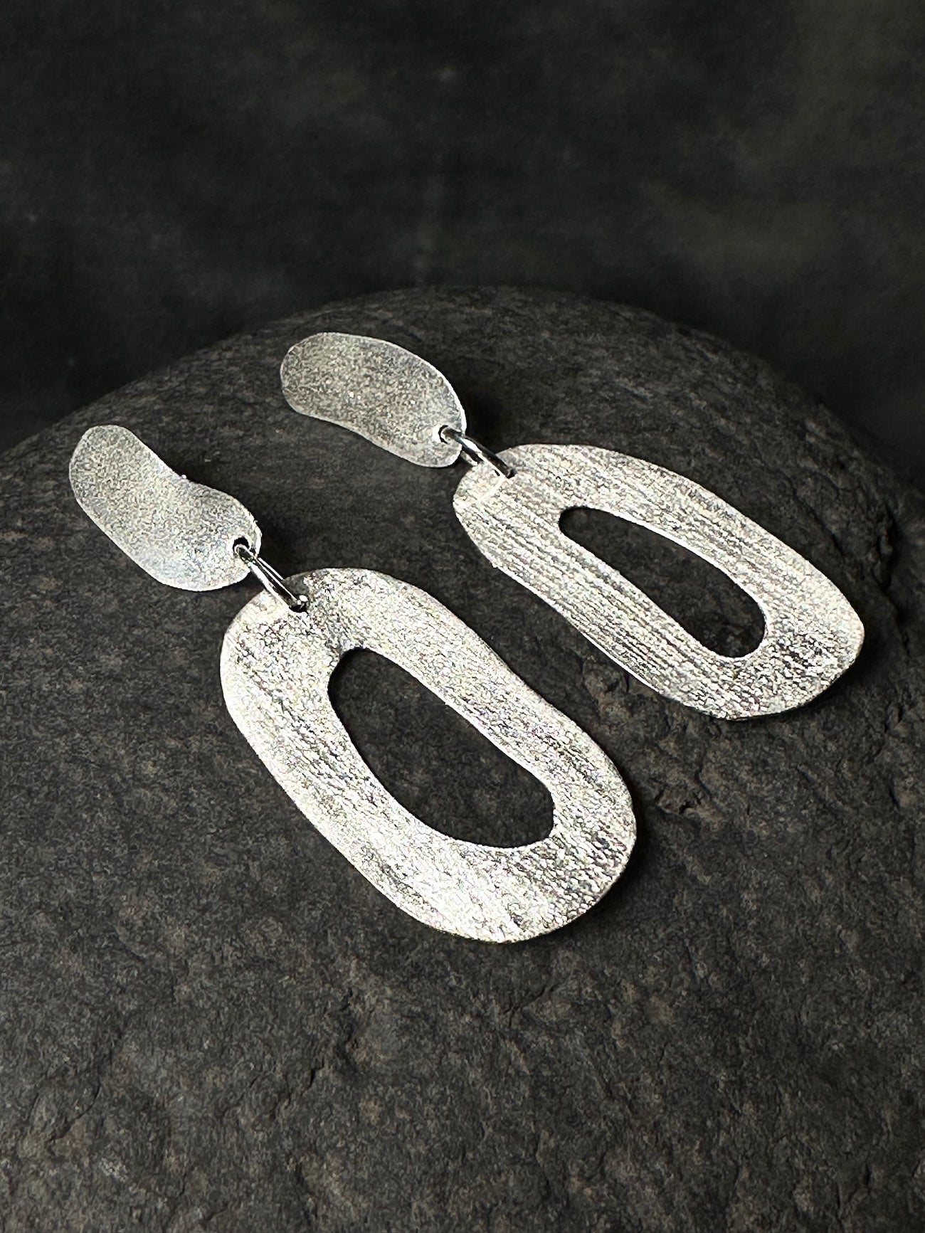 Close-up of textured sterling silver statement earrings showing hand-forged finish