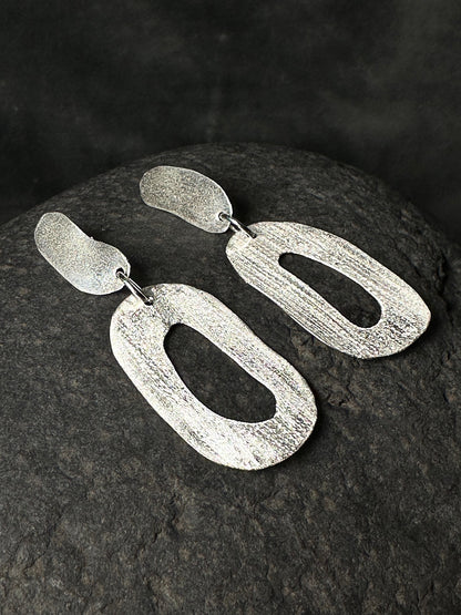 Close-up of textured sterling silver statement earrings showing hand-forged finish
