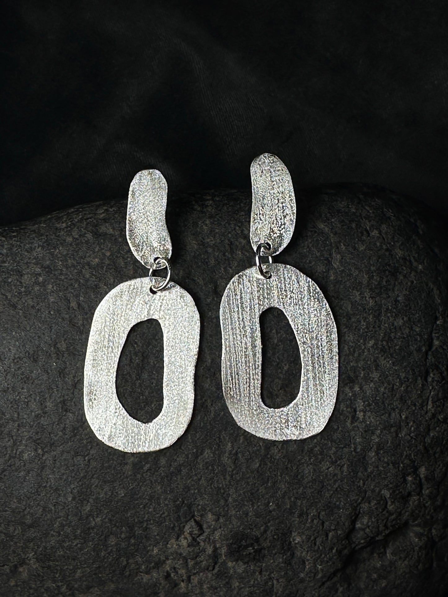 Hammered sterling silver oval link drop earrings on a dark stone background
