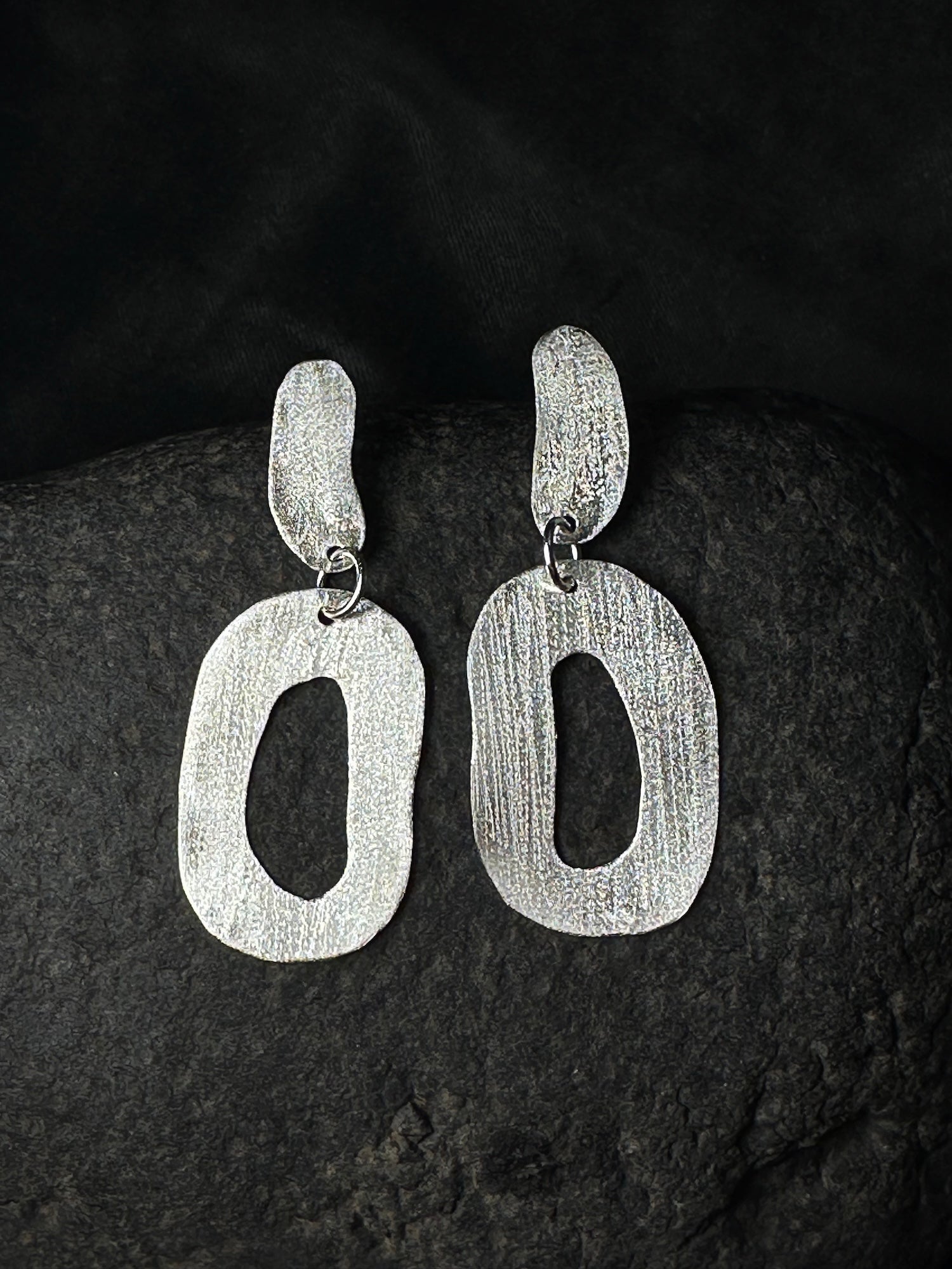 Hammered sterling silver oval link drop earrings on a dark stone background

