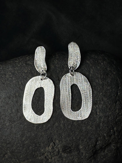 Hammered sterling silver oval link drop earrings on a dark stone background
