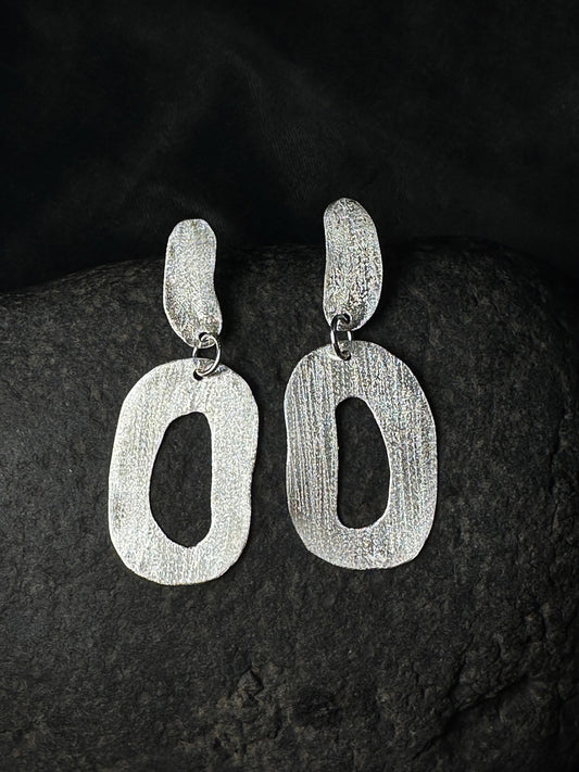 Hammered sterling silver oval link drop earrings on a dark stone background
