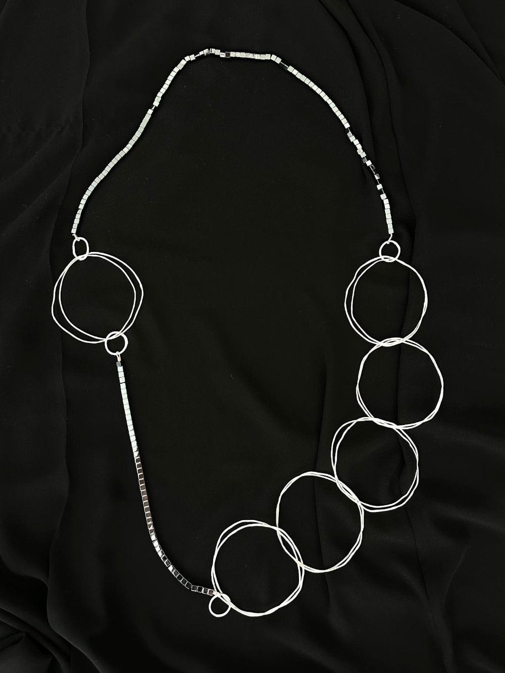 Extra long statement necklace with hammered silver rings and hematite cubes laid flat