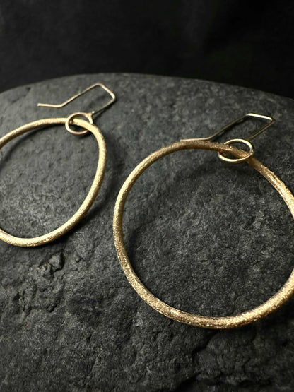 Macro detail of hand-textured surface on small gold hoop earrings