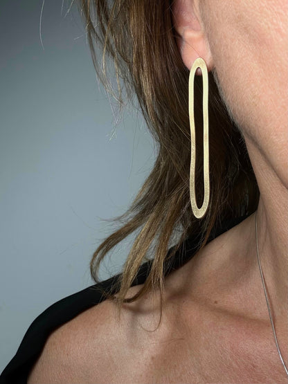 Model wearing large gold oval hoop earring, close-up