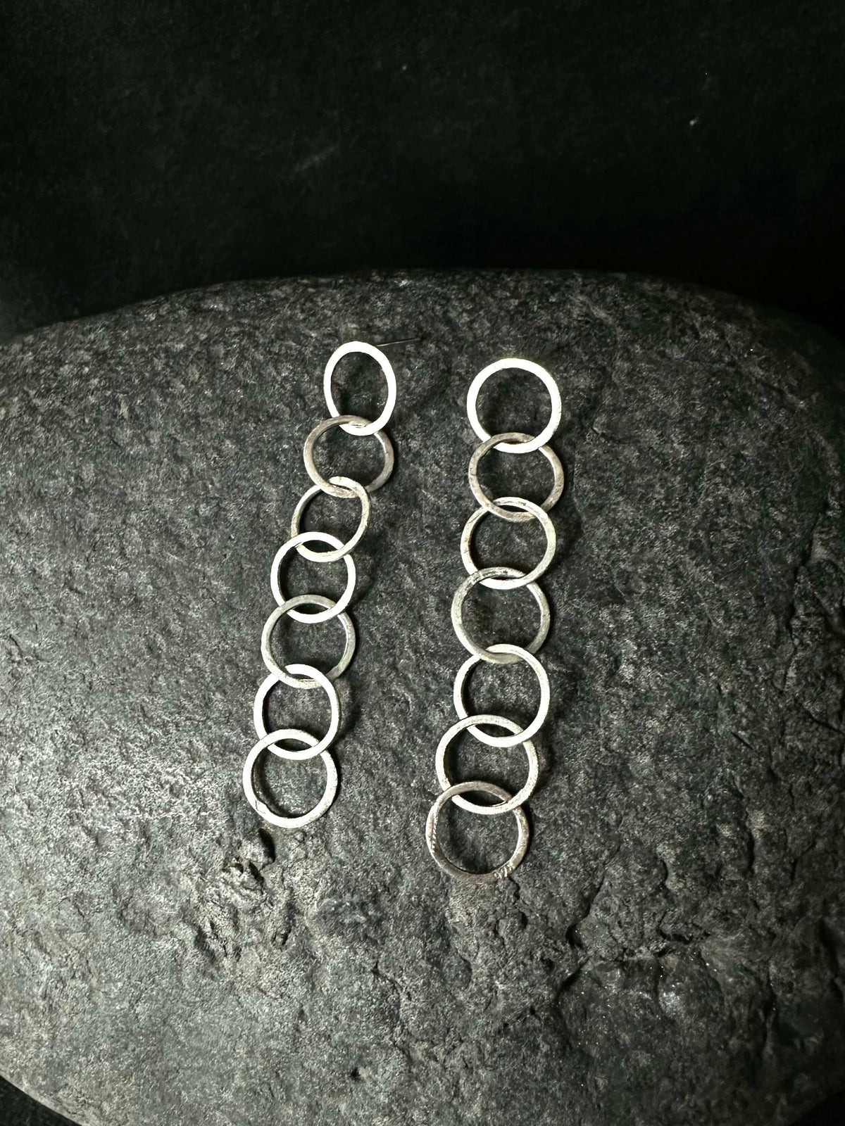 Pair of silver loop chain drop earrings laid on a dark stone