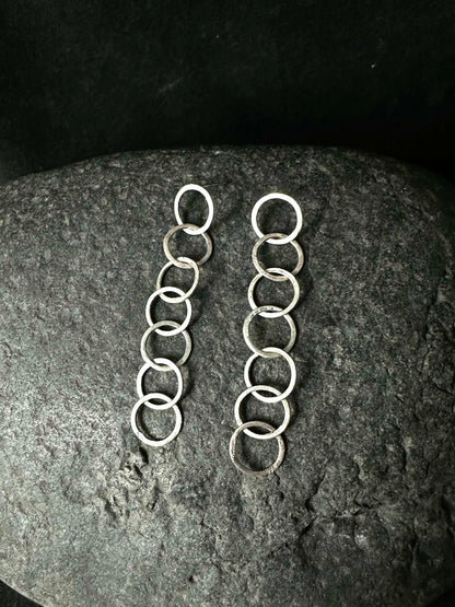 Pair of silver loop chain drop earrings laid on a dark stone