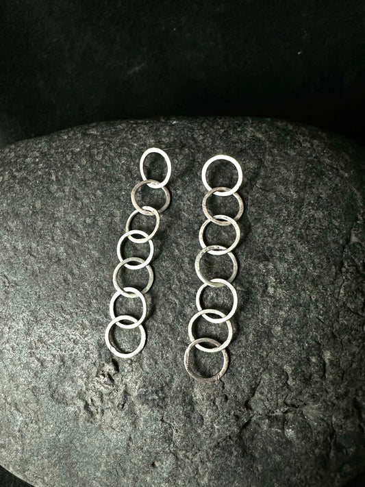 Pair of silver loop chain drop earrings laid on a dark stone