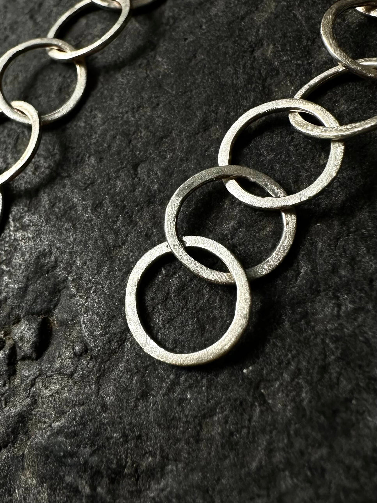 Close-up of hand-hammered sterling silver circle links, textured finish, on dark stone