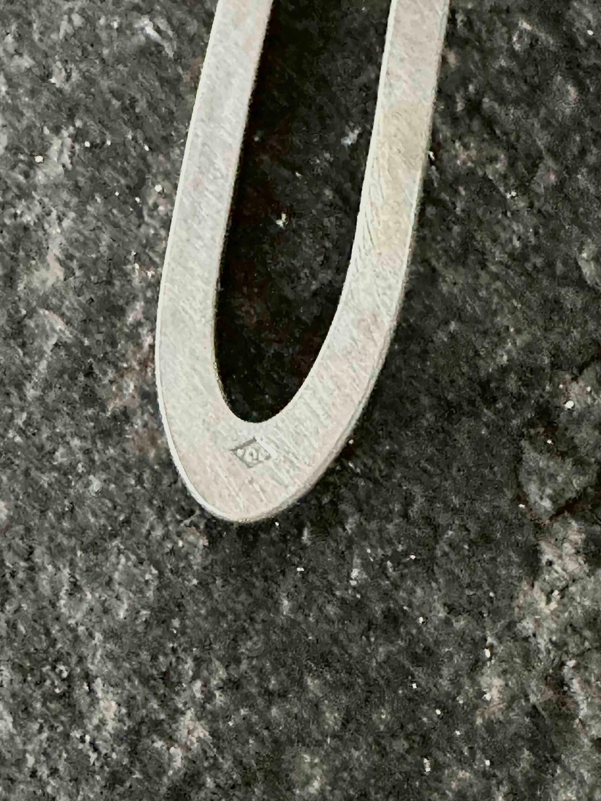 Close-up of a hand-stamped poinçon de maître hallmark on a sterling silver oval drop