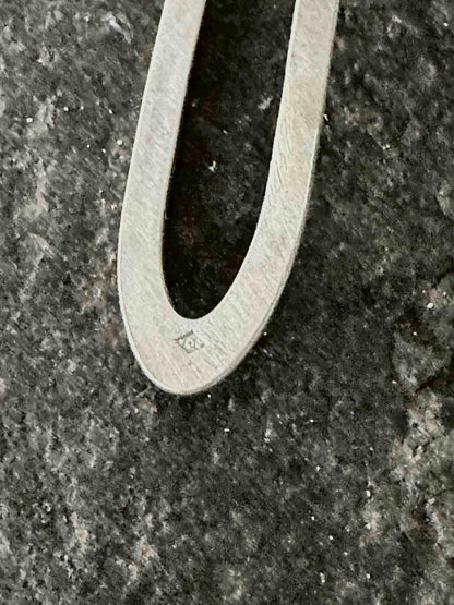 Close-up of a hand-stamped poinçon de maître hallmark on a sterling silver oval drop