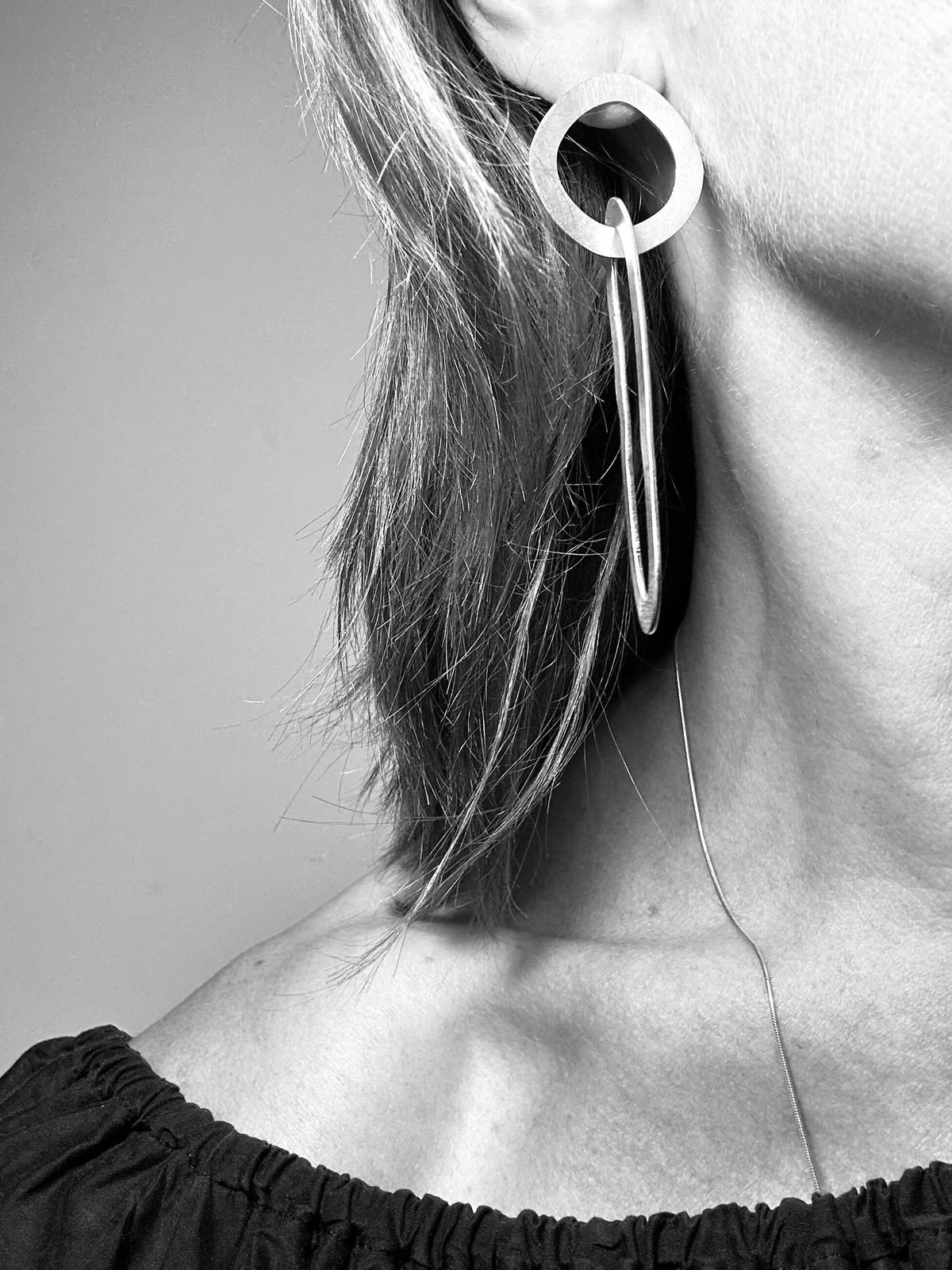 Black and white photo of long brushed silver circle and oval link statement earrings worn on the ear