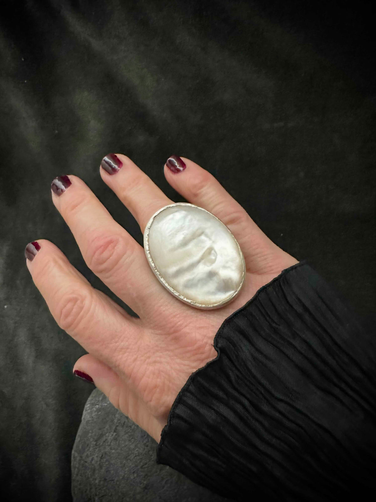 Mother of pearl cocktail ring worn on hand with dark red nails