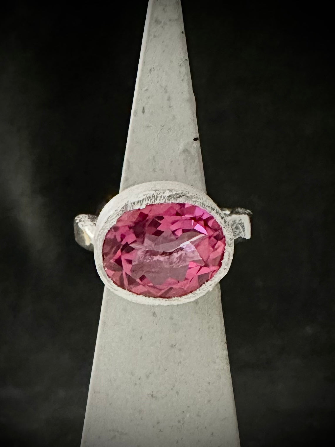 Faceted oval pink topaz ring in a brushed silver bezel on a ring cone