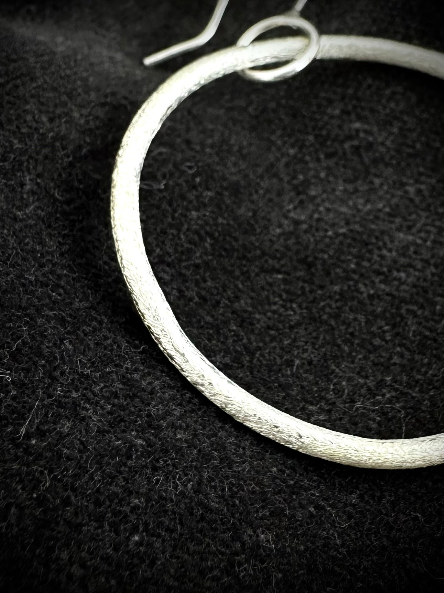 Close-up of handmade textured sterling silver hoop earring showing ear wire and organic finish
