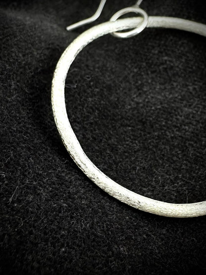 Close-up of handmade textured sterling silver hoop earring showing ear wire and organic finish
