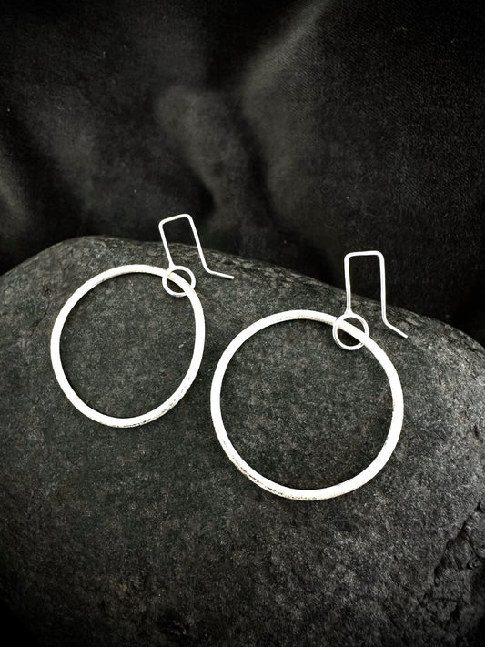 Pair of handmade textured sterling silver dangly hoop earrings, 4cm diameter, on dark stone