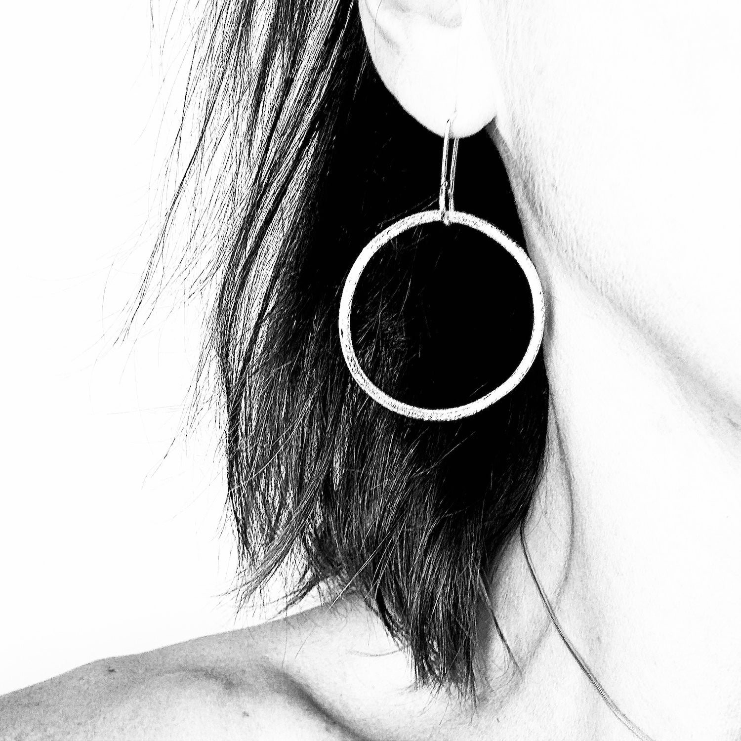 Woman wearing handmade textured sterling silver dangly hoop earring, black and white styled photo