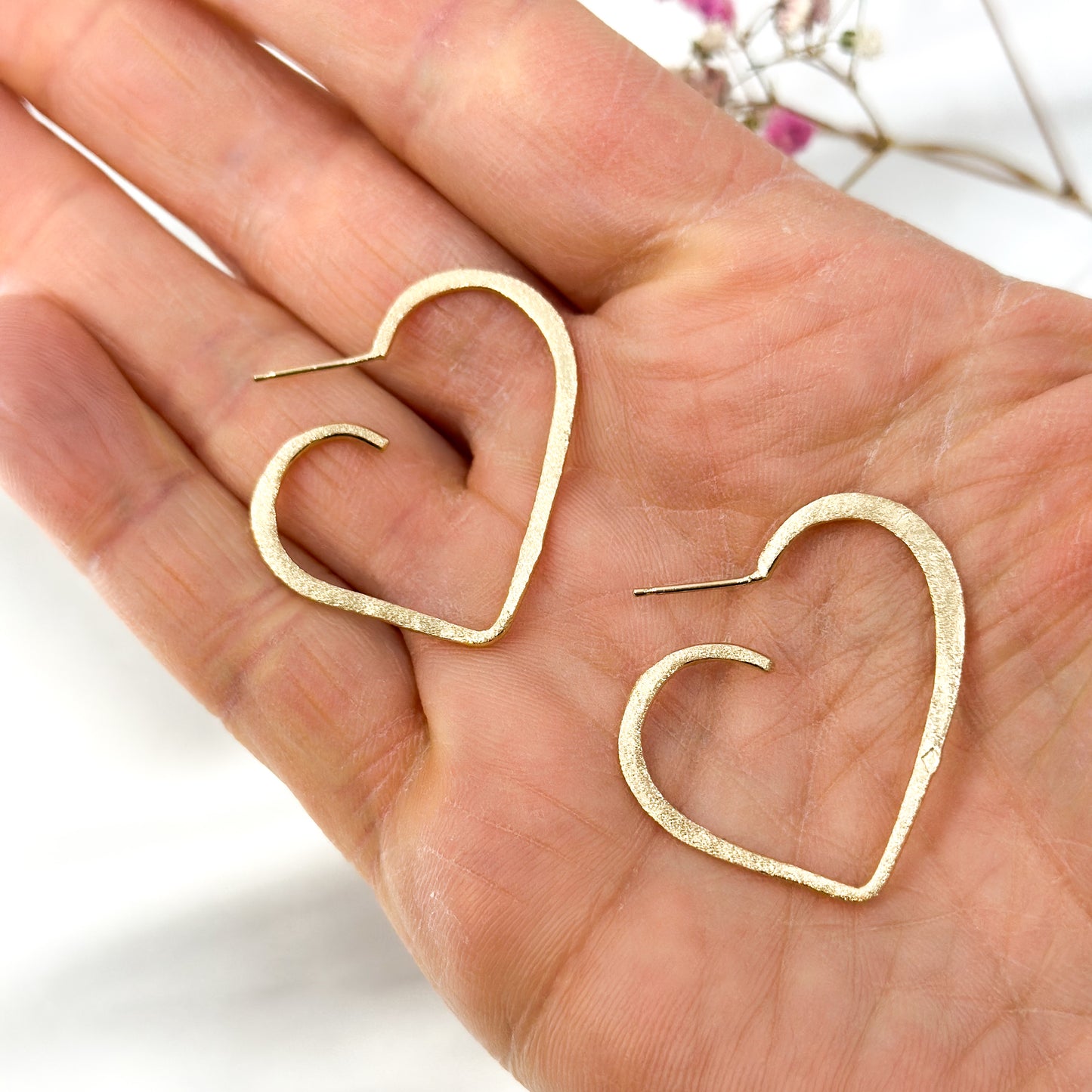 Gold-plated open heart stud earrings in 925 sterling silver, shown on hand
