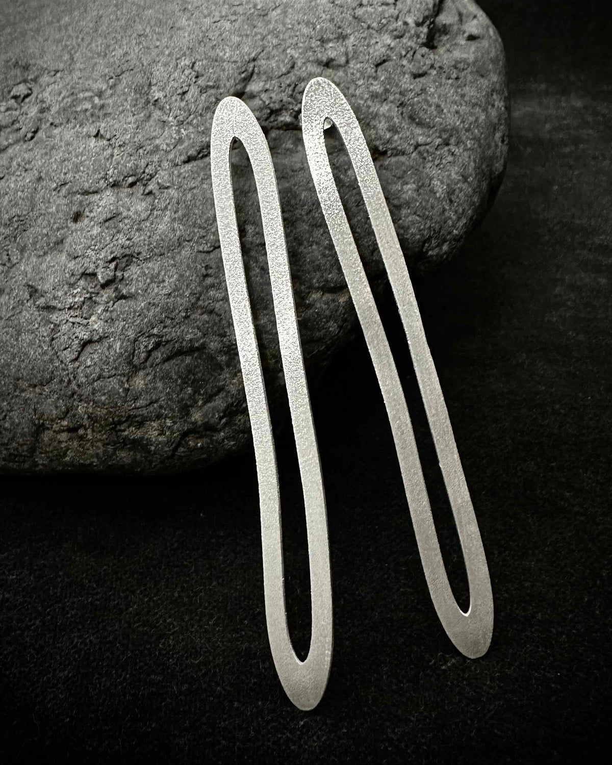 Long oval silver paperclip earrings laid on dark stone - minimalist handmade jewelry
