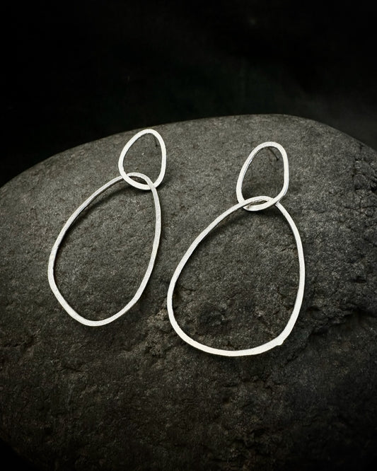 Minimalist sterling silver drop earrings with organic sculptural shapes on dark stone background