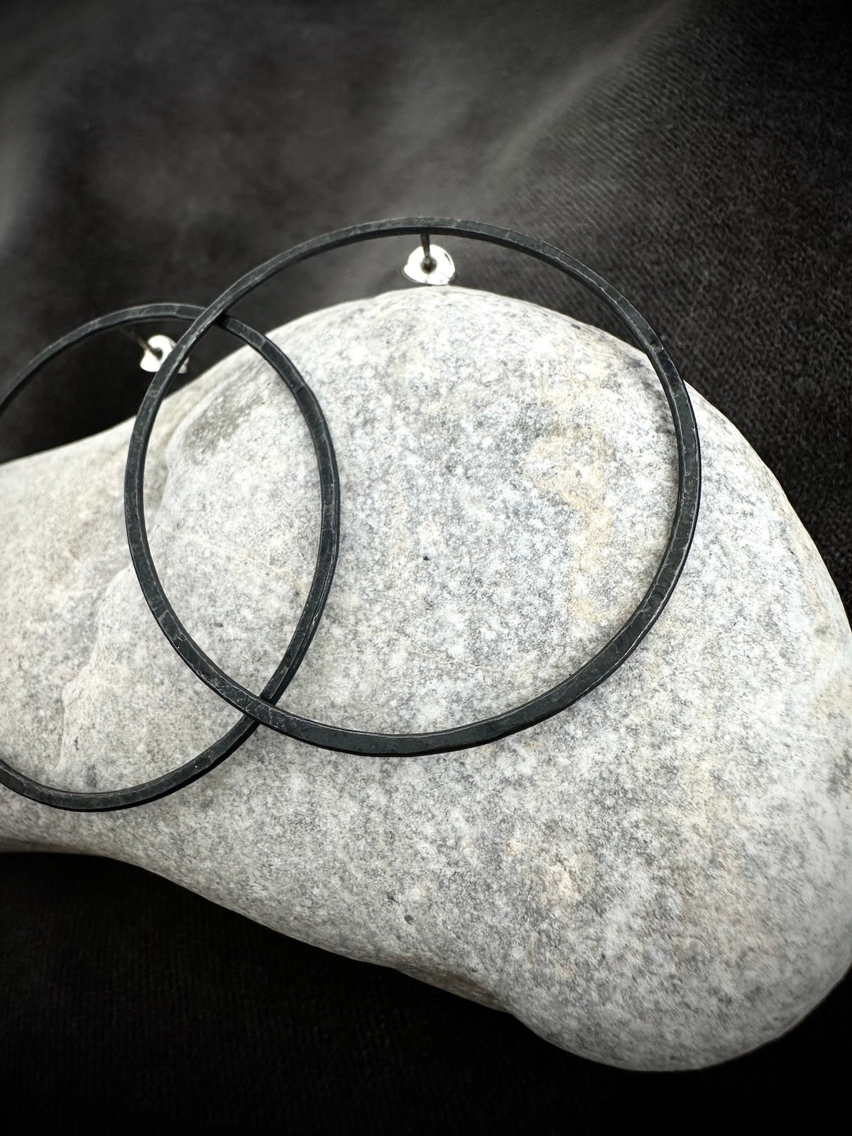Black oxidised silver hoop earrings resting on stone - large round hoops