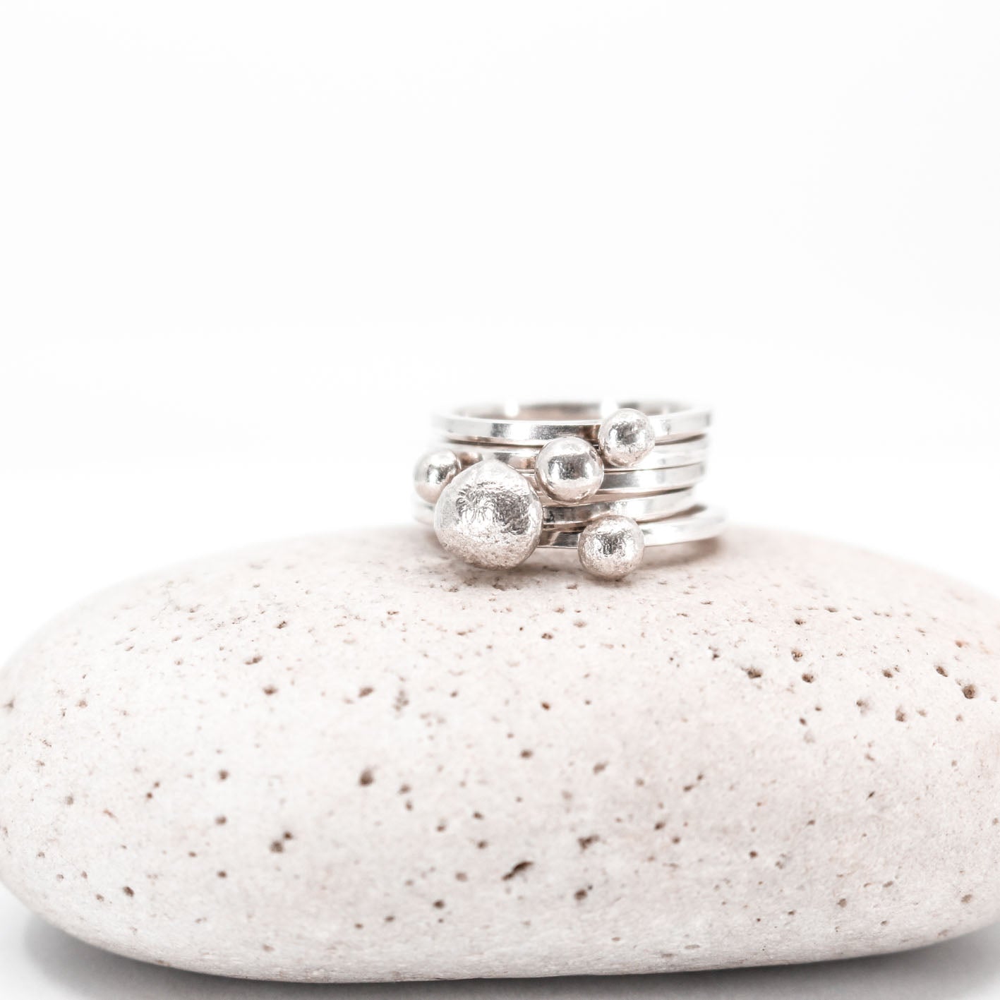 five simple silver stacking rings each with a textured sterling silver drop