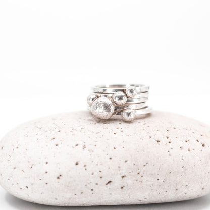 five simple silver stacking rings each with a textured sterling silver drop