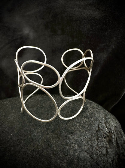 One-of-a-kind sculptural sterling silver cuff bangle with textured overlapping loops, on dark stone